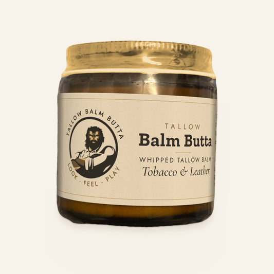 Tallow Roots Co. Tobacco & Leather Balm Butta whipped tallow balm in a glass jar with gold lid and cream label, front view on a plain cream background