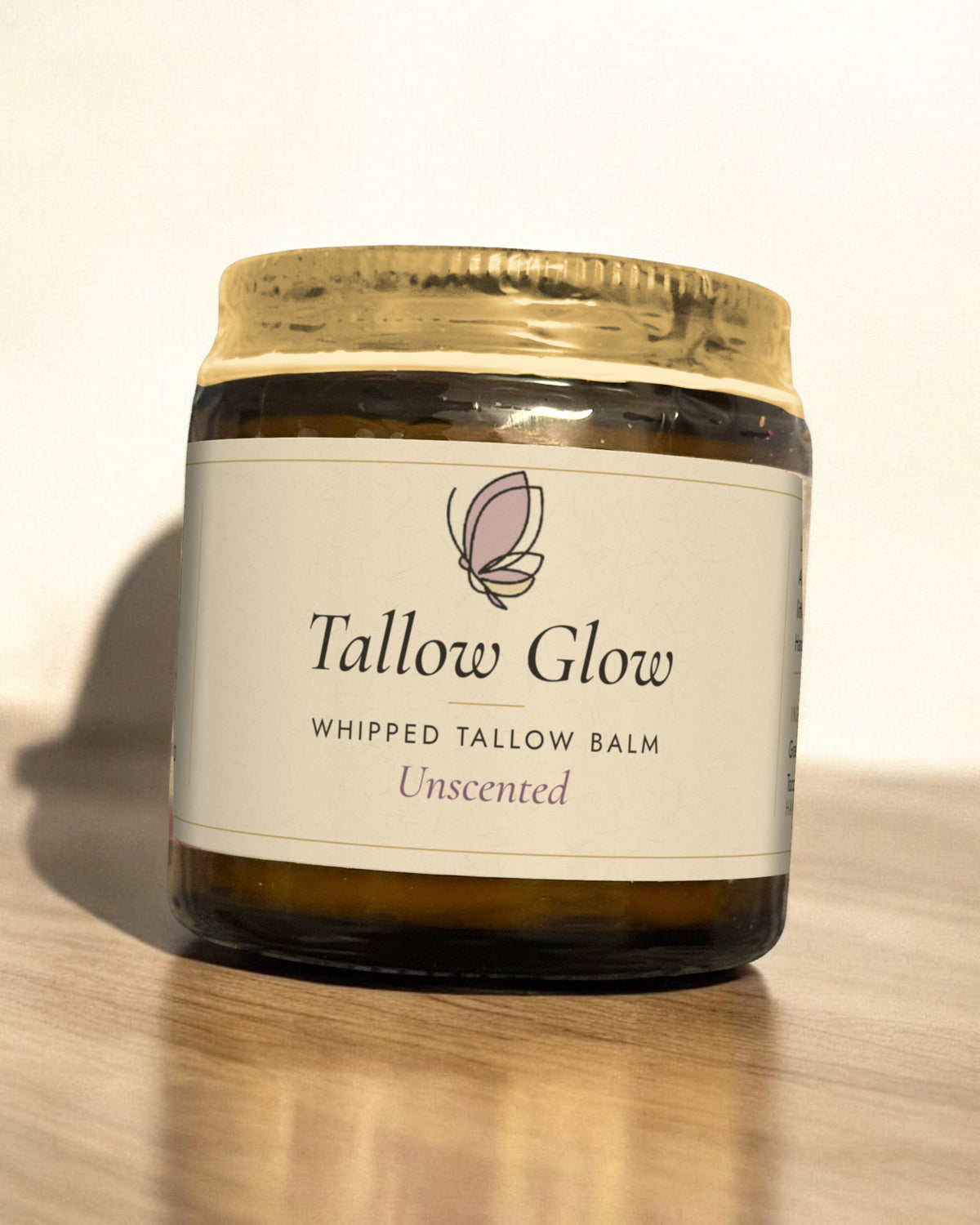 Tallow Roots Co. Unscented Tallow Glow whipped tallow balm in a glass jar with gold lid and cream label, sitting on a wooden shelf against a plain wall
