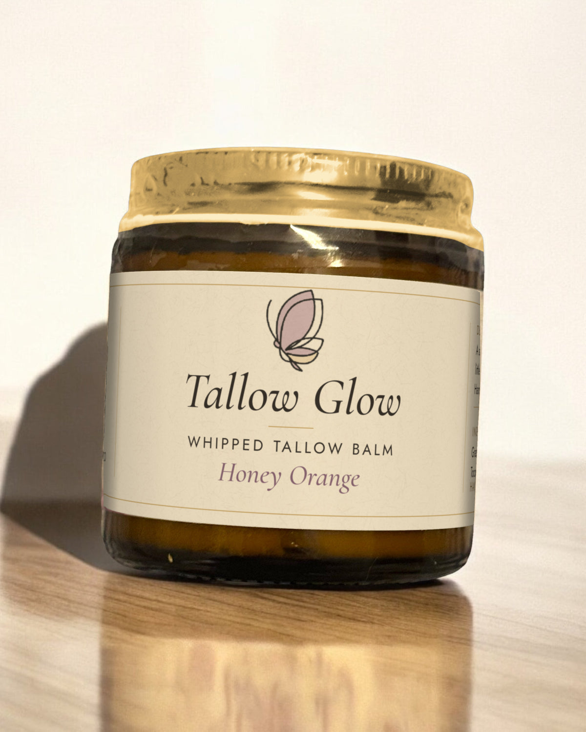 Tallow Roots Co. Honey Orange Tallow Glow whipped tallow balm in a glass jar with gold lid and cream label, sitting on a wooden shelf against a plain wall